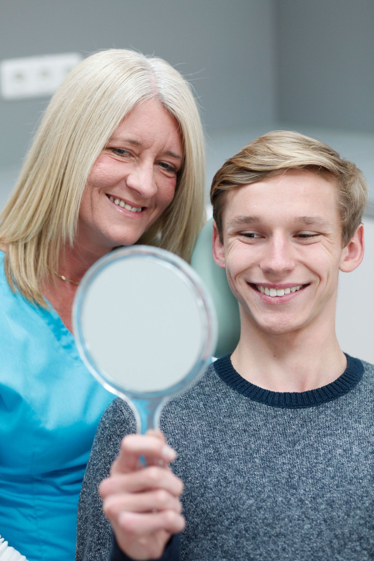 Patient betrachtet lächelnd das Ergebnis nach einem Bleaching im Spiegel